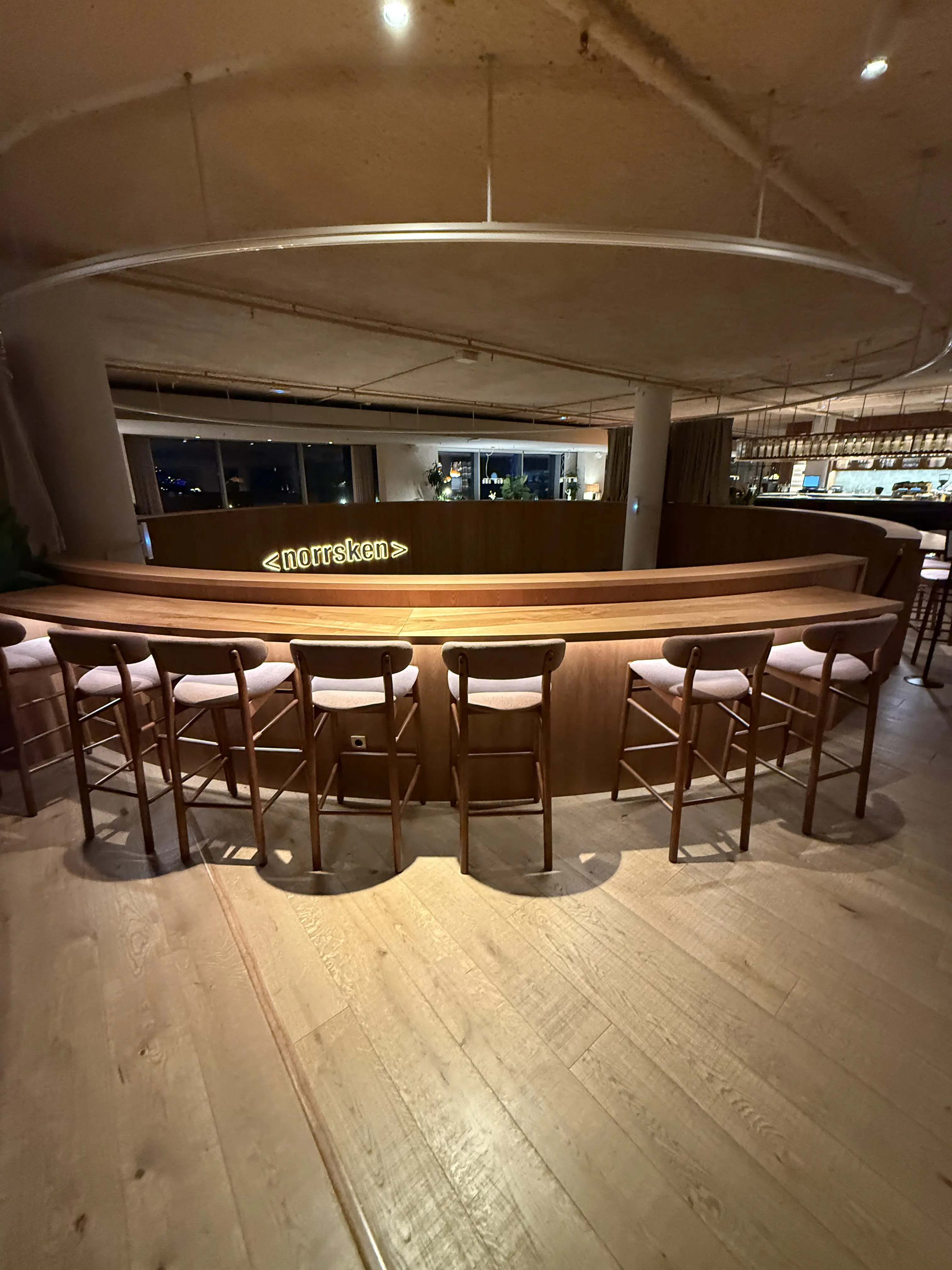 Norrsken House Barcelona rooftop bar at night with curved wooden counter and neon sign