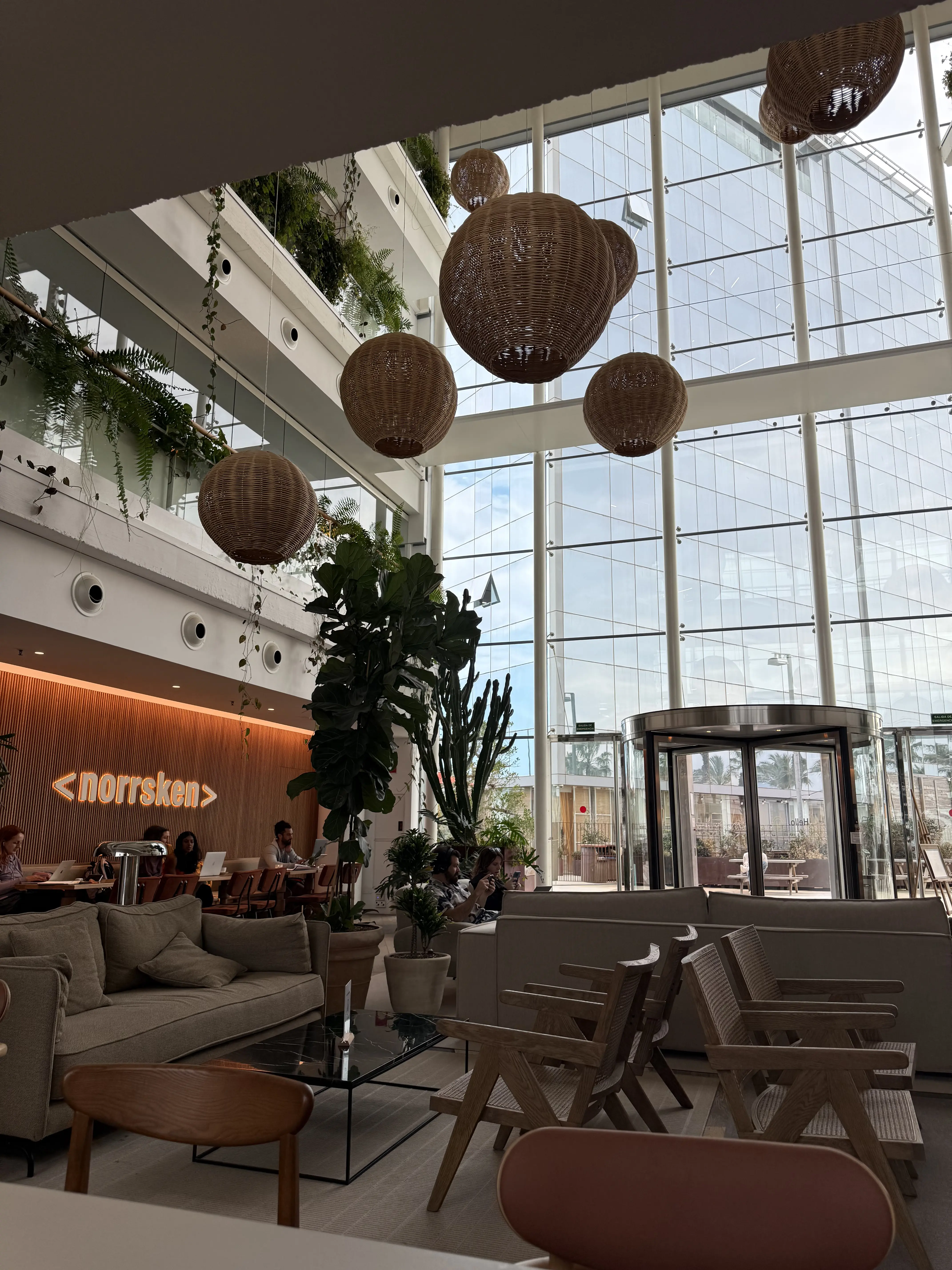 Norrsken House Barcelona bright atrium with rattan pendant lights and neon sign